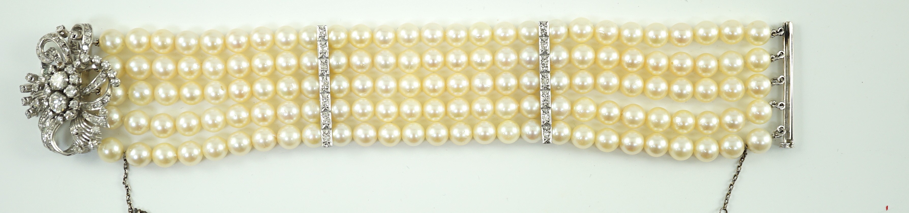 A mid to late 20th century continental quintuple strand cultured pearl bracelet, with white gold and diamond cluster set scroll clasp and diamond set line spacers